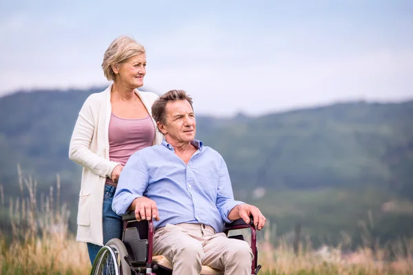 Seniorin schiebt Mann im Rollstuhl, grüne Herbstnatur — Stockfoto