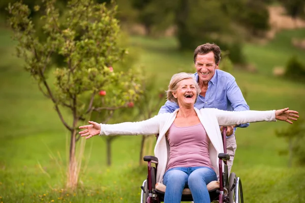 Hombre mayor empujando a la mujer en silla de ruedas, naturaleza verde otoño — Foto de Stock