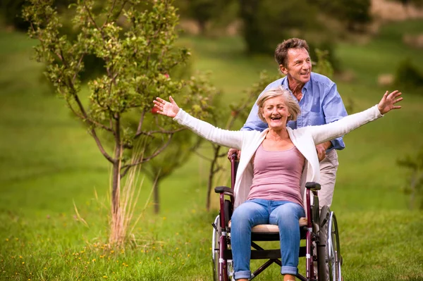 Старший мужчина толкает женщину в инвалидной коляске, зеленая осенняя природа — стоковое фото