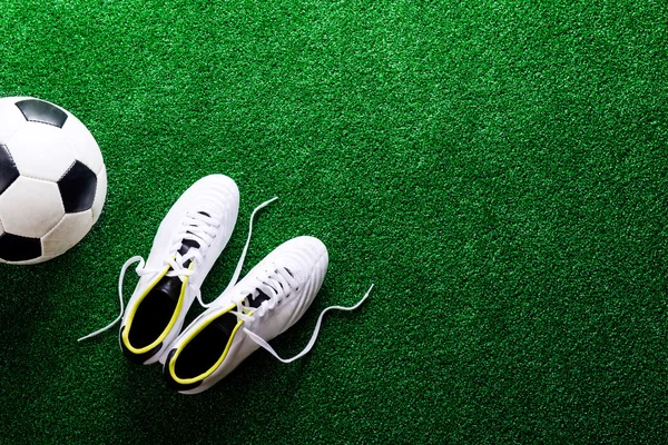 Soccer ball and cleats against green artificial turf, studio sho — Stock Photo, Image