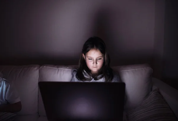 Niña, sentada en una oscuridad, jugando con el portátil — Foto de Stock