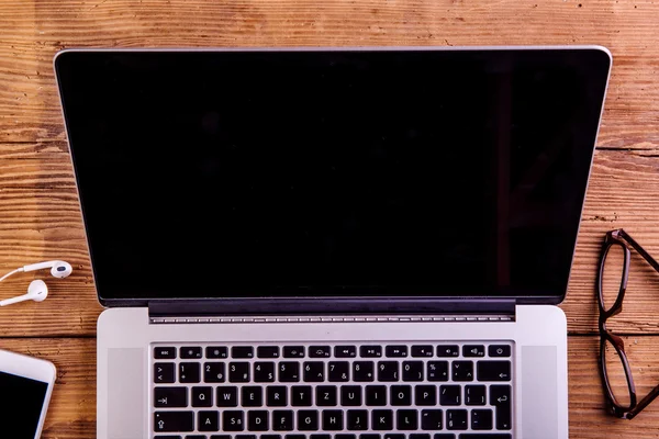 Laptop, smartphone, earphones and eyeglasses laid on office desk — Stock Photo, Image