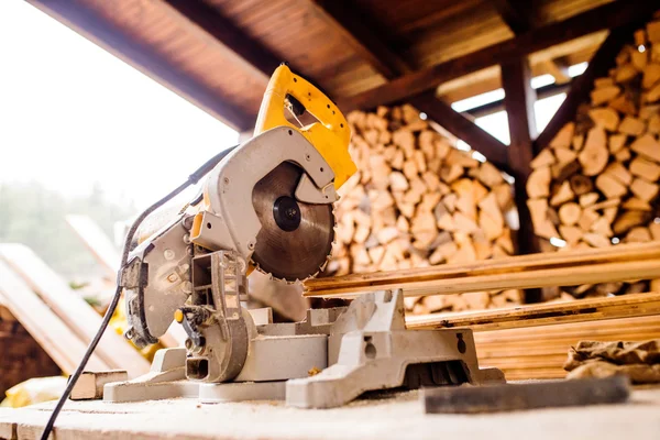 Circular saw laid on table, stack of wood behind it — Stock Photo, Image