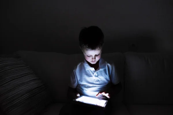 Niño pequeño, sentado en una oscuridad, jugando con la tableta — Foto de Stock