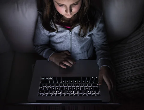 Niña, sentada en una oscuridad, jugando con el portátil — Foto de Stock