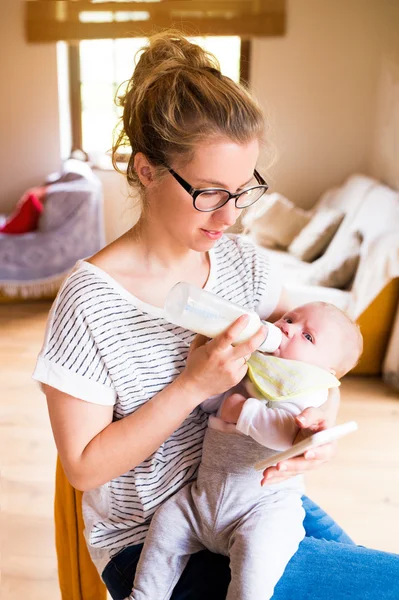 Ibu cantik memberi makan bayi laki-laki, susu dalam botol, smartphone — Stok Foto
