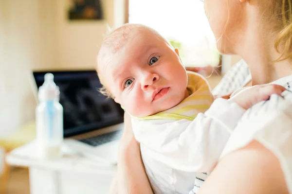 Mère méconnaissable tenant bébé fils, lait dans le biberon, ordinateur portable — Photo