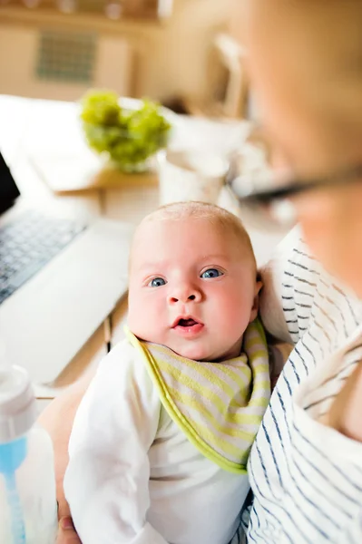 Unrecognizable mother holding baby son, laptop on table, close u