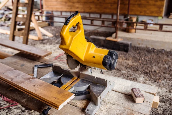 Circular saw laid on table, stack of wood behind it — Stock Photo, Image