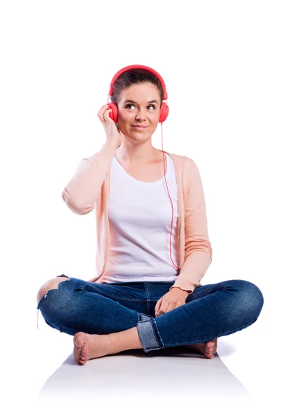 Woman with earphones sitting on the floor, studio shot, isolated — Stock Photo, Image