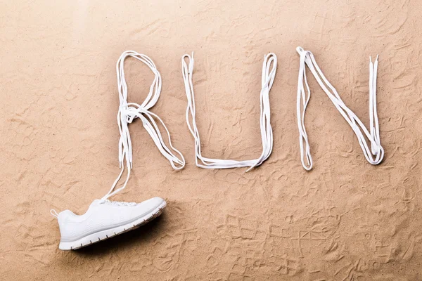 Running shoe and run sign made of shoelaces, sand