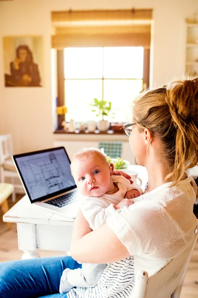 Beautiful mother holding baby son, laptop on table, close up — Stock Photo, Image
