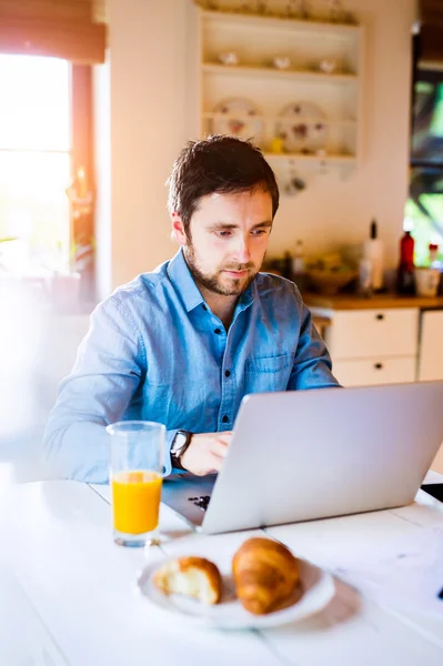 Homem sentado na mesa trabalhando em casa no laptop — Fotografia de Stock