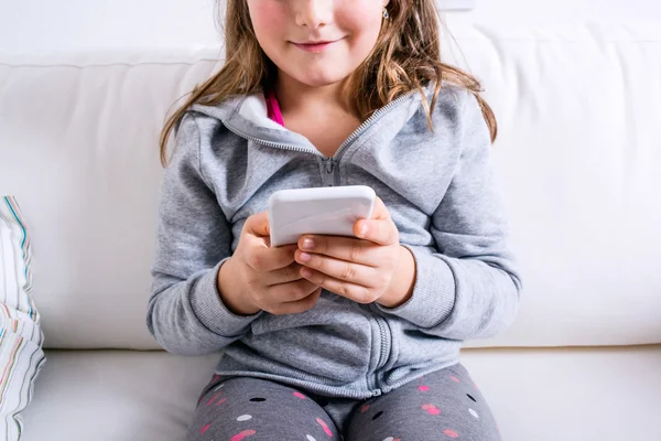 Unrecognizable little girl sitting on sofa, playing with smartph — Stock Photo, Image