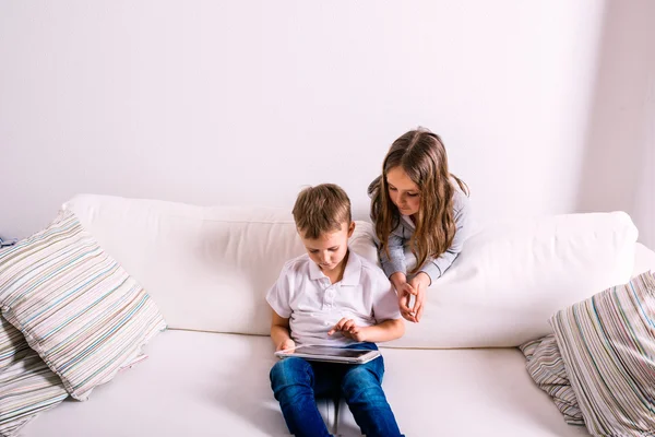 Crianças em casa sentadas no sofá, brincando com tablet — Fotografia de Stock
