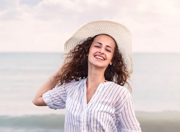 Donna in spiaggia con camicia e cappello, sorridente, con la testa in mano — Foto Stock