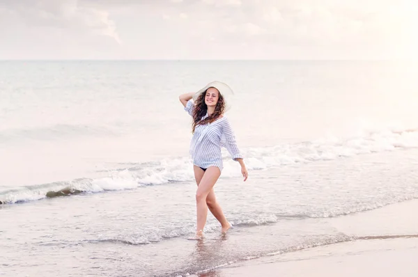 Mulher na praia vestindo camisa e chapéu, sorrindo, segurando a cabeça — Fotografia de Stock