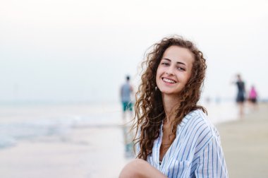 Beyaz gömlekli, sahilde oturan güzel kadın gülümseyerek