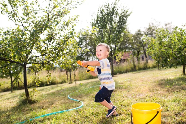 Chlapeček s vodní pistole šplouchání někoho, slunné letní garde — Stock fotografie