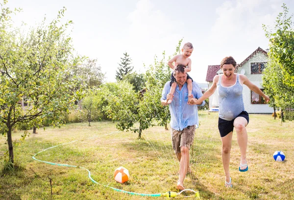 Niño pequeño con madre y padre en el aspersor — Foto de Stock