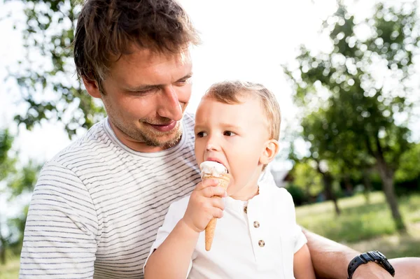 Far och son äter glass, solig sommarträdgård — Stockfoto