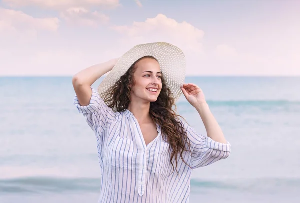 Donna in spiaggia con camicia e cappello, sorridente, con la testa in mano — Foto Stock