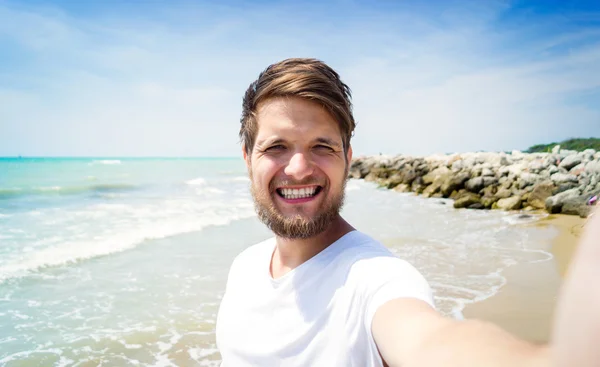 Hipster mannen på stranden, leende, med selfie, solig sommar — Stockfoto