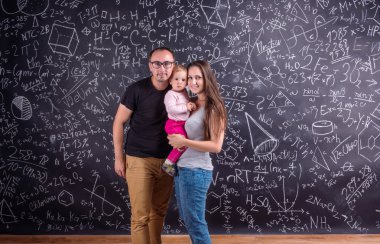 Young family with little daughter against big blackboard