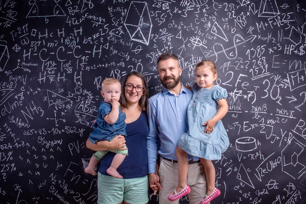 Giovane famiglia con due piccole figlie contro grande lavagna — Foto Stock
