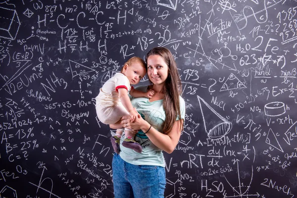 Jovem mãe com pequena filha contra grande quadro negro — Fotografia de Stock