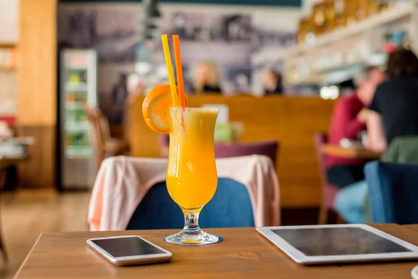 Pomarańczowy napój, tablet, smartfon ułożona na stole w kawiarni — Zdjęcie stockowe