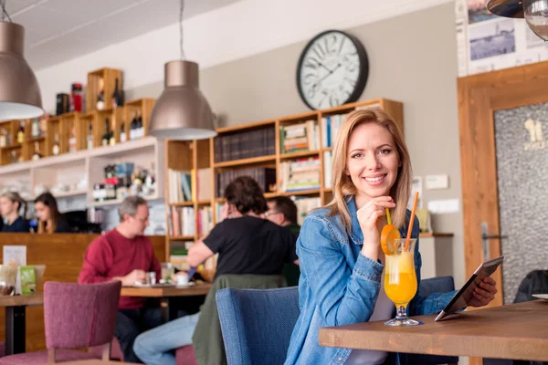 Young woman in cafe with drink, holding tablet — Stock Photo, Image