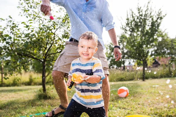 Malý chlapec s otcem hrál s vodní děla, šplouchání — Stock fotografie