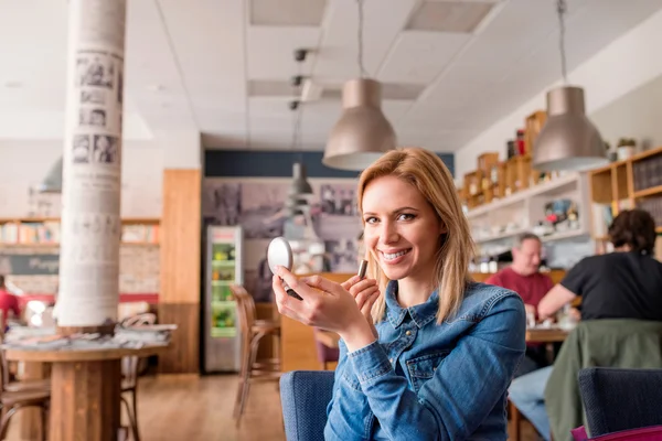 Giovane donna in caffè che si mette il rossetto guardando in uno specchio — Foto Stock