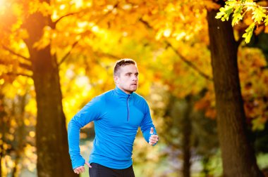 Young handsome athlete running outside in sunny autumn nature
