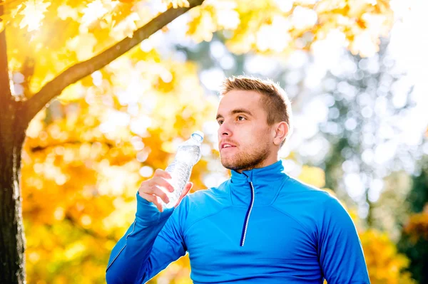 Hipster runner in herfst natuur drinkwater uit fles — Stockfoto