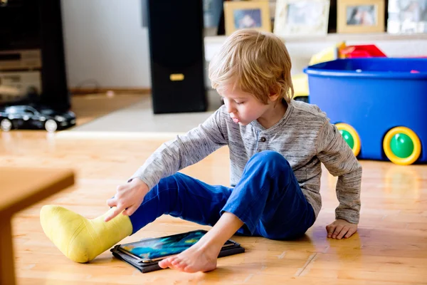 Boy with broken leg  playing on tablet. — Stock Photo, Image