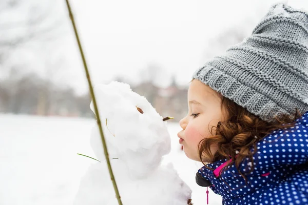 Little girl kissing a snowman in winter nature — Stock Photo, Image