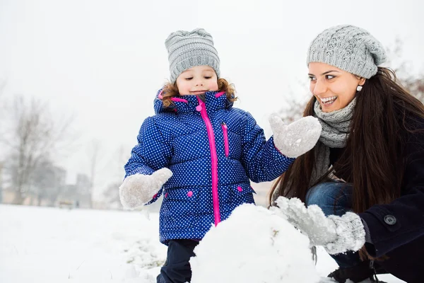 Madre e hija construyendo un muñeco de nieve en la naturaleza invernal —  Fotos de Stock