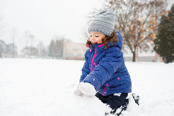 Liten flicka bygga en snögubbe i vinter natur — Stockfoto