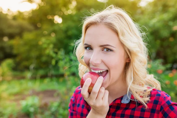 Mooie blonde vrouw in rode ingecheckte shirt eten apple — Stockfoto