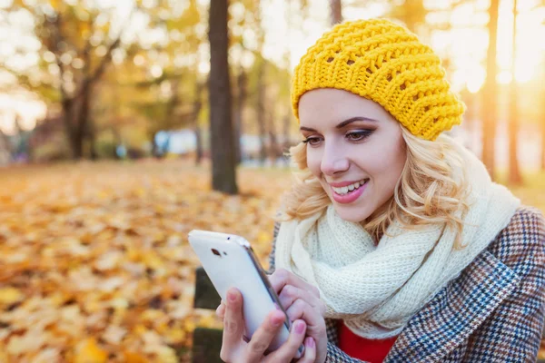 Hermosa mujer con teléfono inteligente en el colorido parque de otoño — Foto de Stock