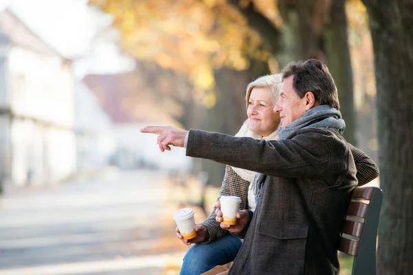 Äldre par sitter på bänken, dricka kaffe. Höstens natur. — Stockfoto