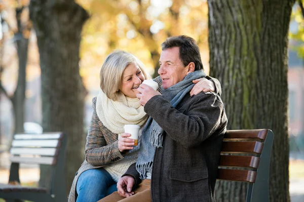Starší pár sedí na lavičce, pití kávy. Podzimní příroda. — Stock fotografie