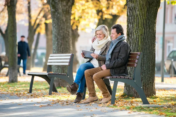 Seniorenpaar mit Tablet auf Bank sitzend. Herbstpark. — Stockfoto