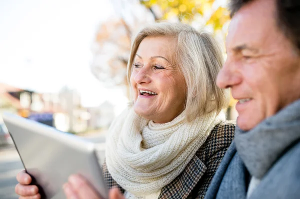 Senior couple with tablet sitting on bench. Autumn park. — Stock Photo, Image