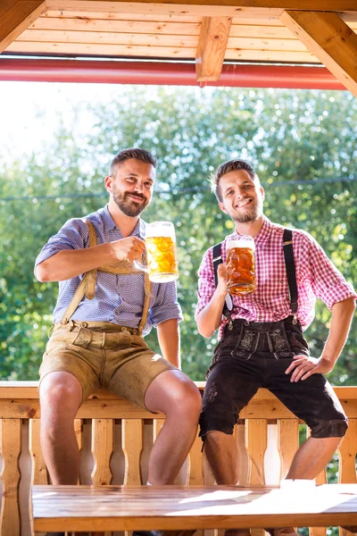 Män i traditionella bayerska kläder håller muggar öl — Stockfoto