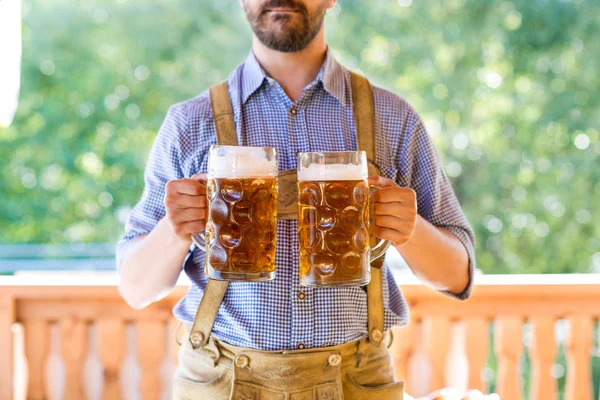 Homem de roupas tradicionais da Baviera segurando canecas de cerveja — Fotografia de Stock