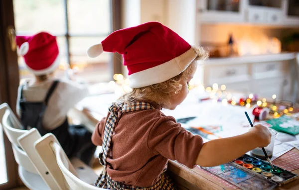 Achteraanzicht van kleine meisje en jongen binnen thuis met Kerstmis, schilderij foto 's. — Stockfoto