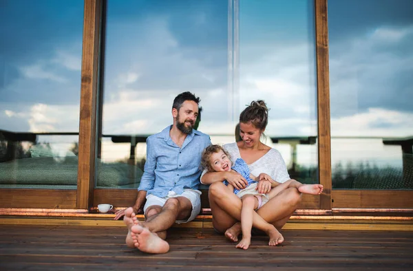 Rodina s malou dcerou sedí na terase dřevěné kabiny, dovolená v přírodě koncept. — Stock fotografie